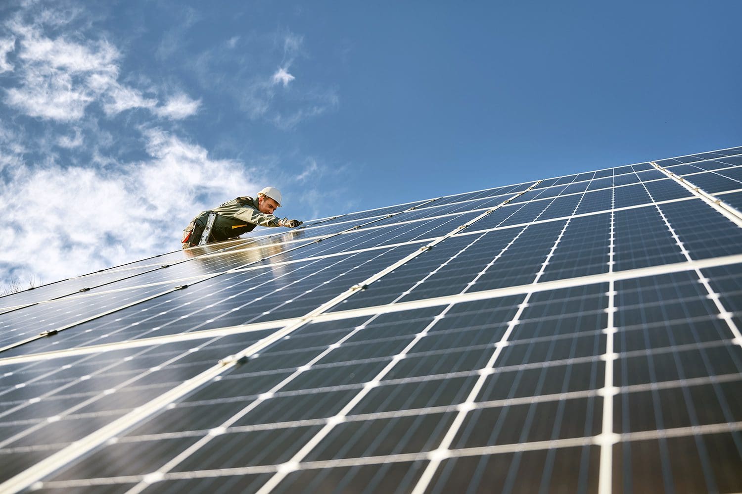 Worker improves corporate sustainability by maintaining solar panels on a roof.